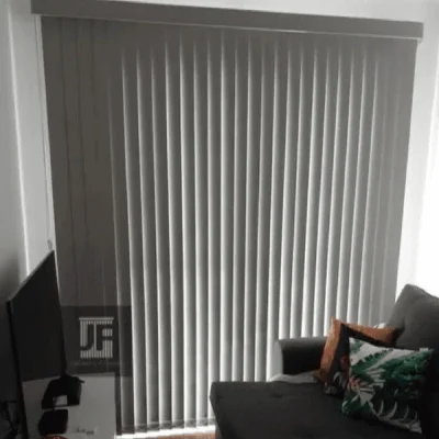 Persiana vertical de tecido instalada em sala moderna com sofá cinza e decoração tropical